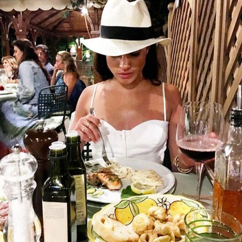 Meghan Markle disfrutando de una comida  acompañada de una copa de vino tinto.